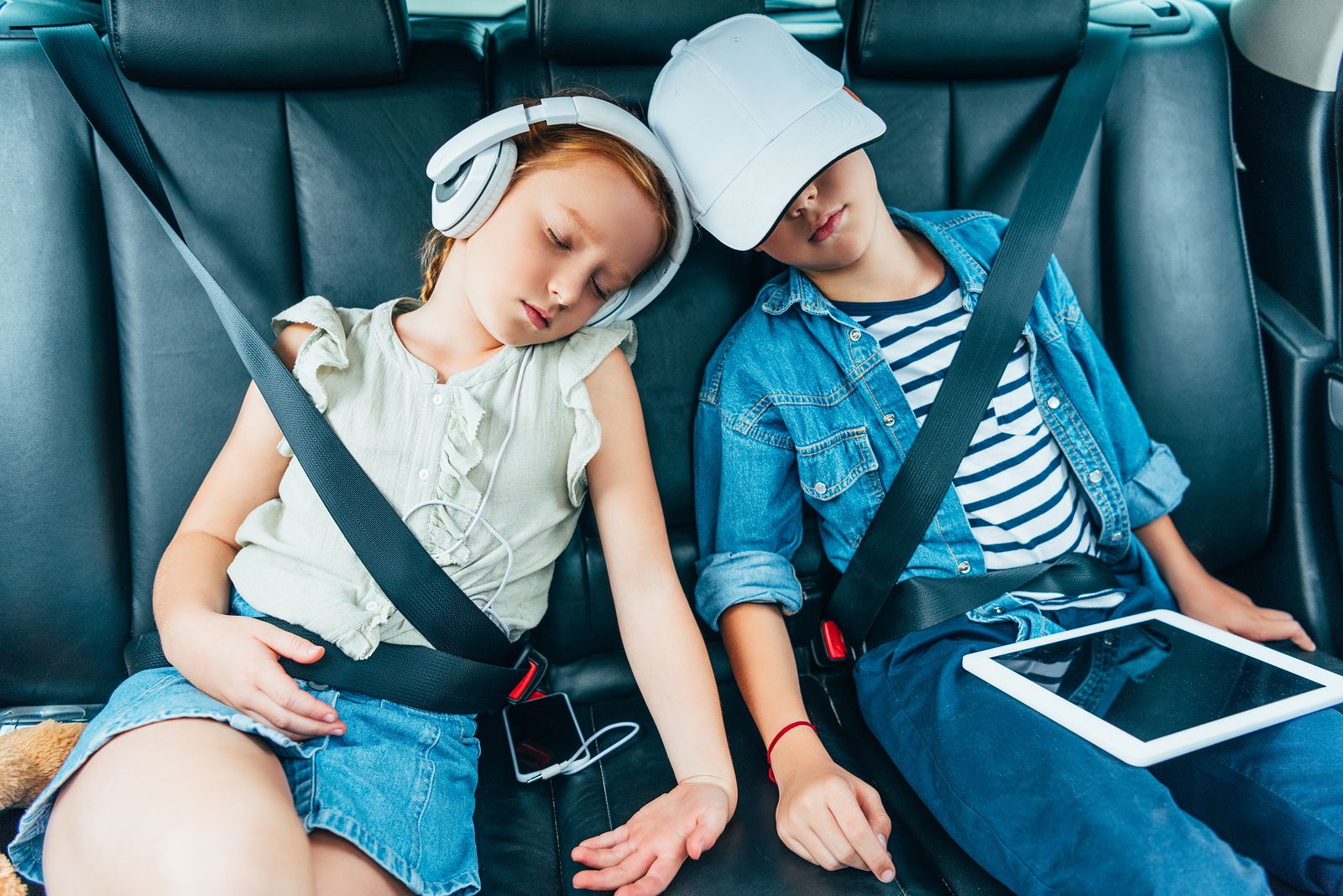 Youngsters asleep in back of car with mobile phone and media pad